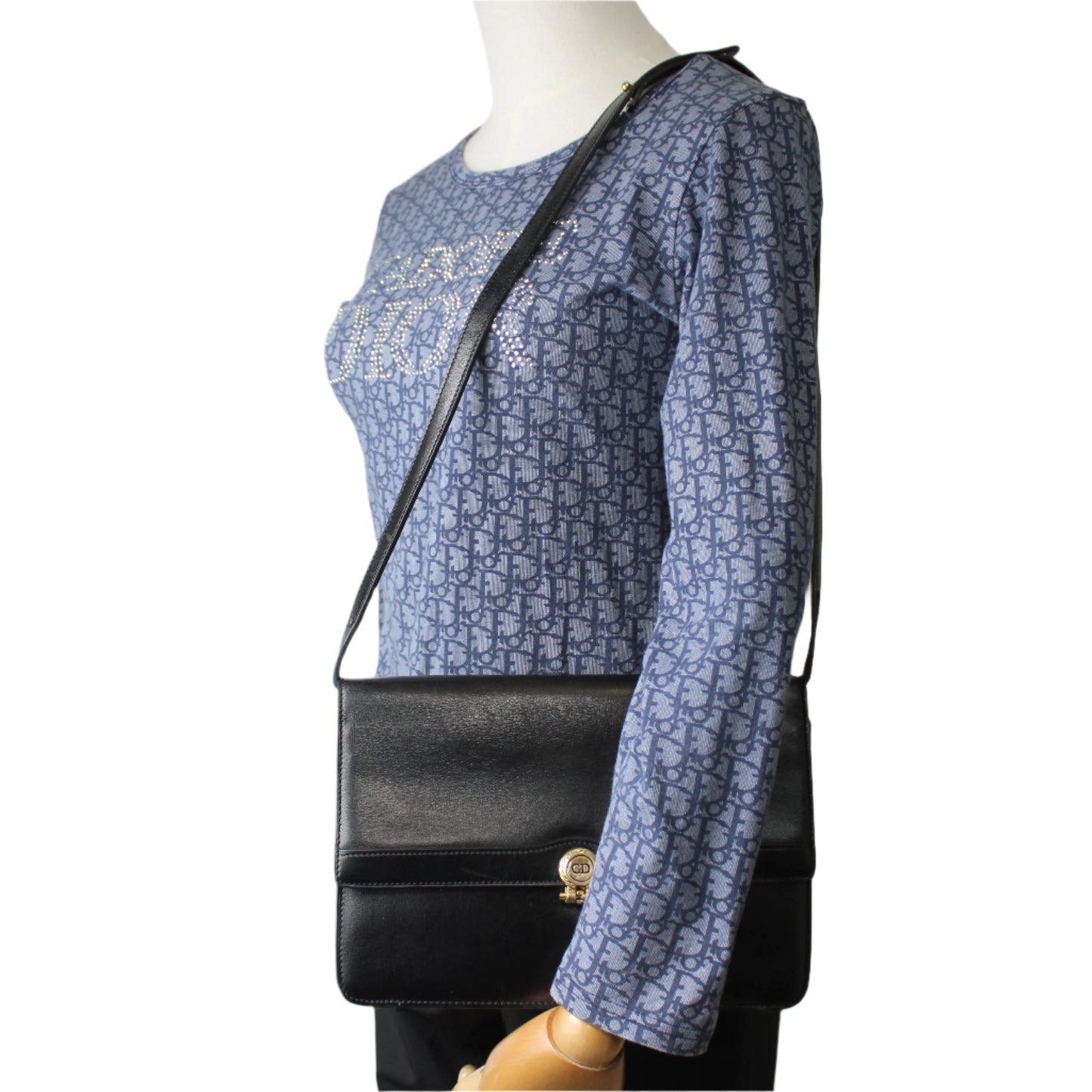 Mannequin wearing a blue patterned dress with a black shoulder bag on a plain background