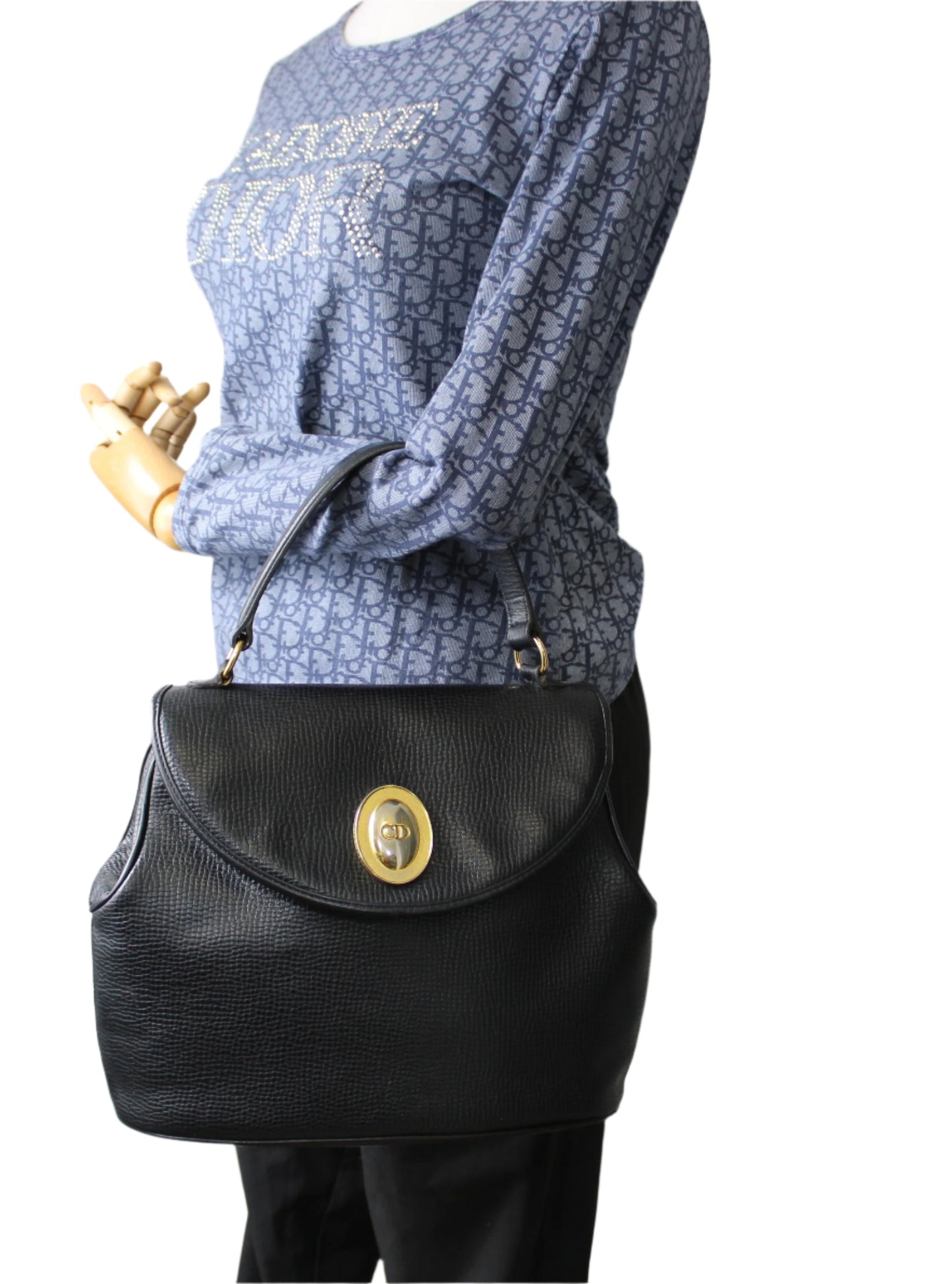 Black handbag with gold clasp on a mannequin against a plain background