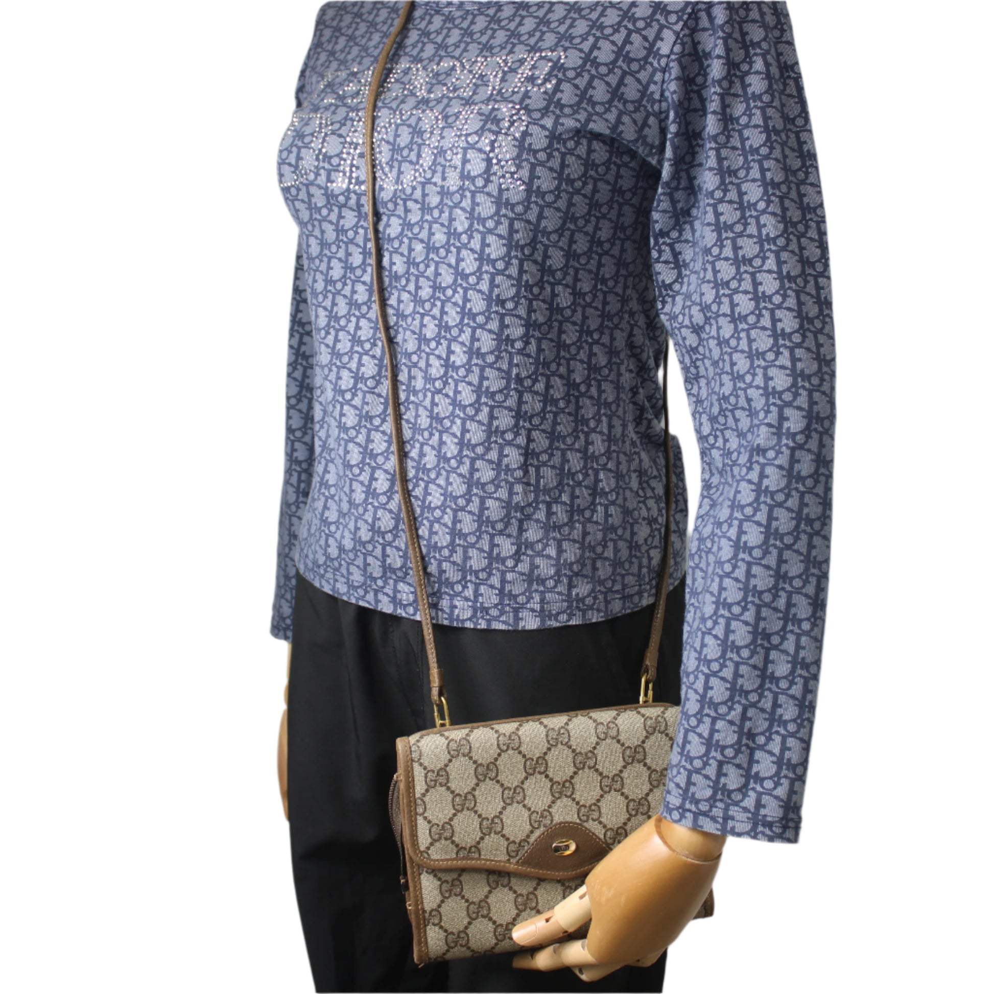 Mannequin wearing a blue patterned shirt holding a brown handbag against a gray background