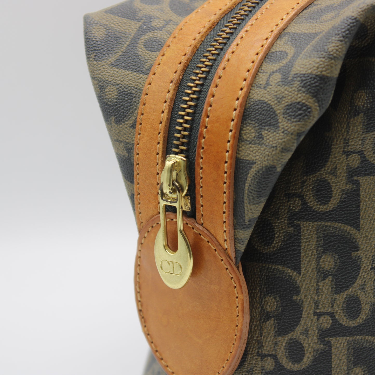 Close-up of a patterned bag with a gold zipper and brown leather pull.