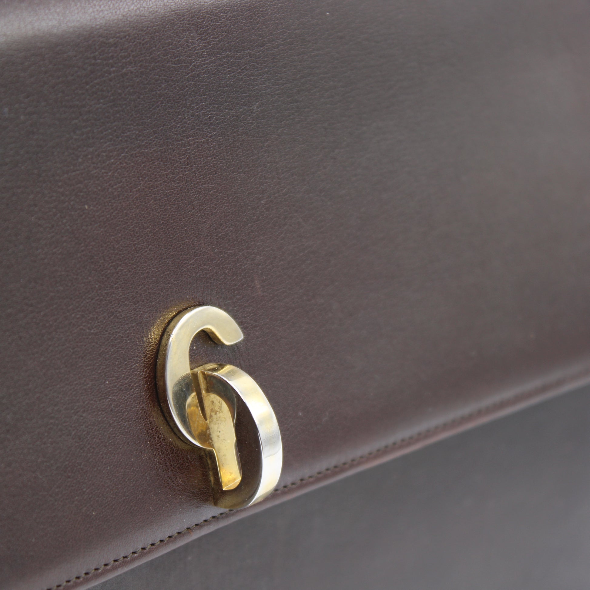 Close-up of a brown leather bag dior t with a gold CD elegant emblem.