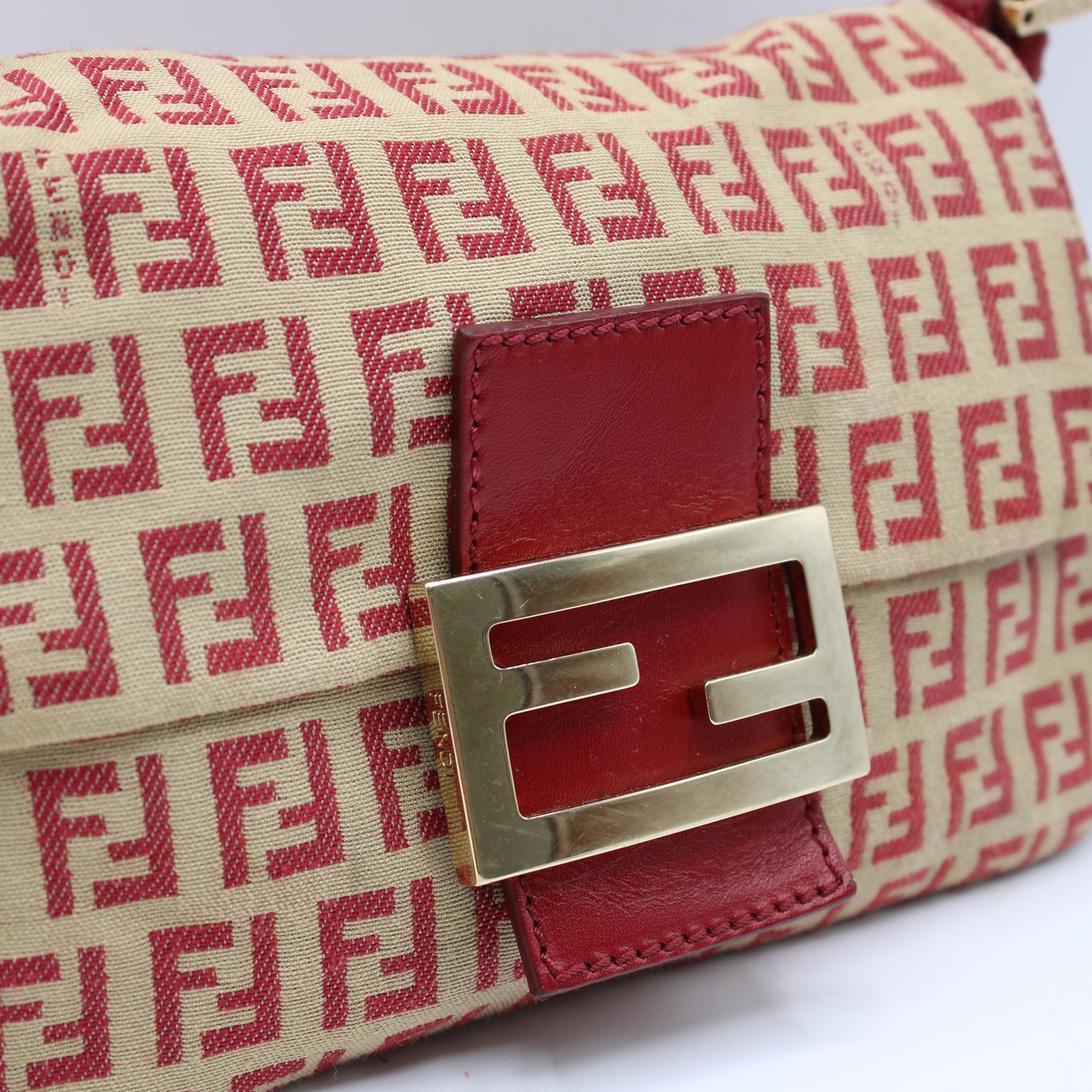 Designer handbag with red and beige pattern and gold clasp on a white background
