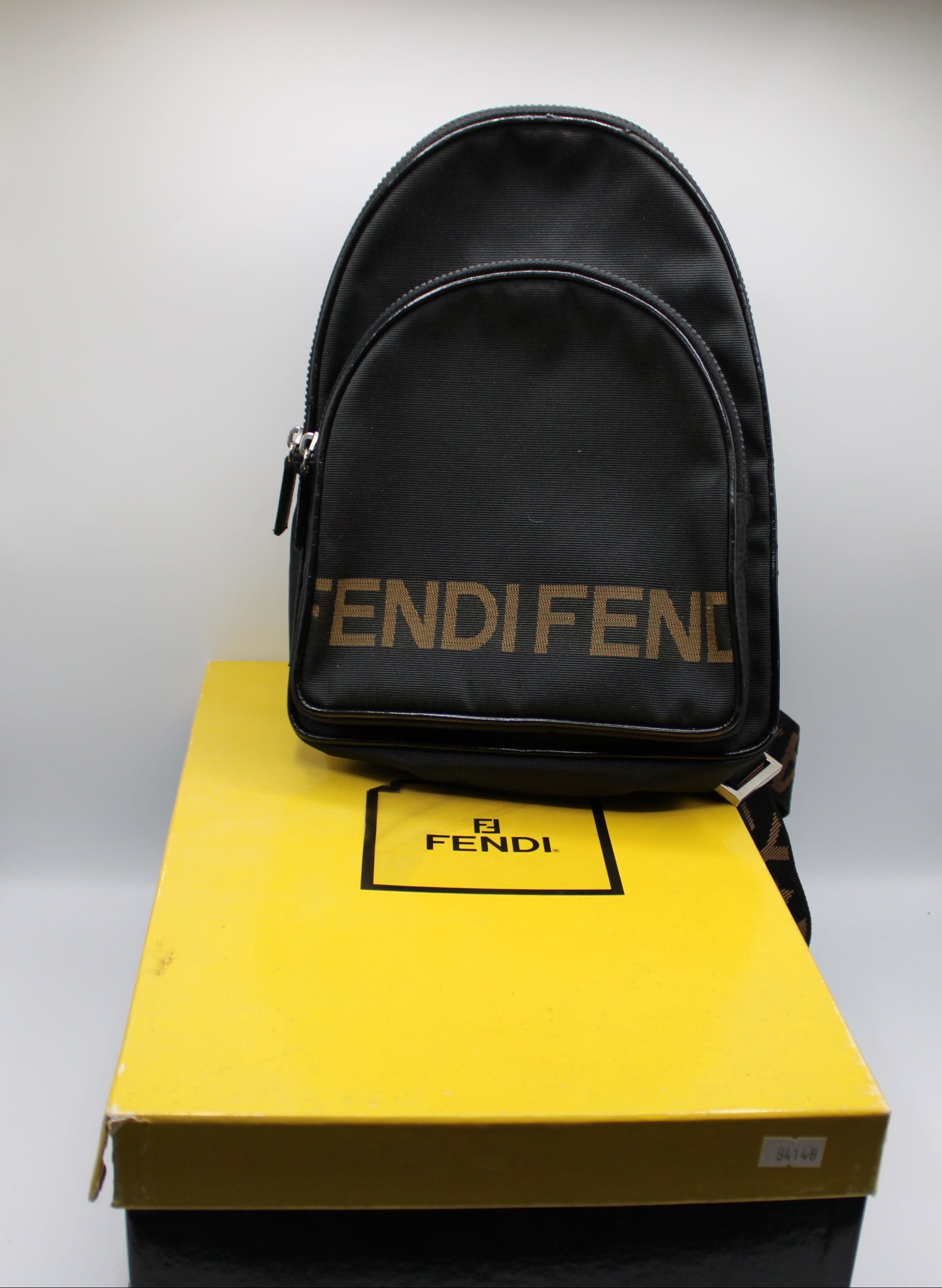 Black Fendi backpack on a yellow Fendi box against a metallic background