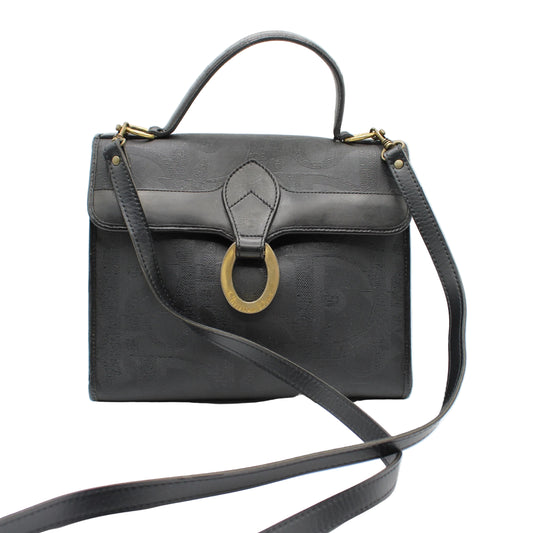 Christian Dior Black Leather Embossed Logo Top Handle Bag Black leather handbag with a gold ring detail on a white background