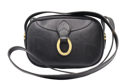 Christian Dior Black Logo Leather Gold Hardware Crossbody Bag A black leather shoulder bag with a tonal monogram pattern, featuring a large gold-tone horsebit ring clasp and a matching black leather strap, shown against a light gray background.