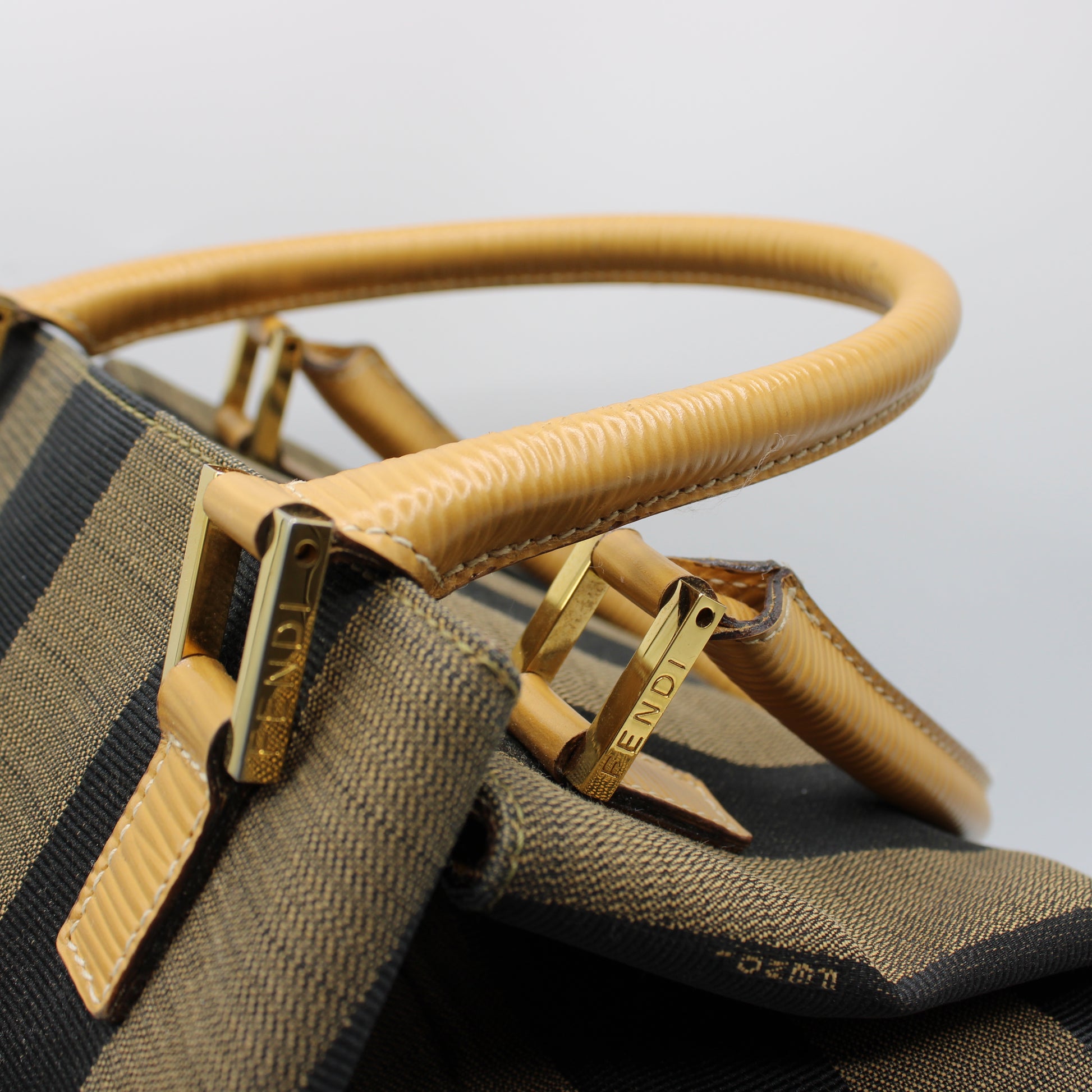 Close-up of a brown handbag with gold accents on a light gray background